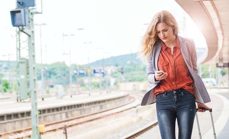 Image of woman with suitcase looking at her phone at train station platform