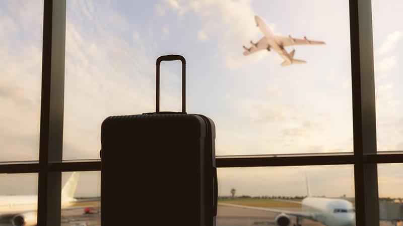 Suitcase at airport with plane taking off